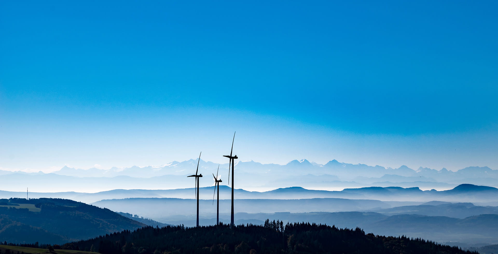 Wind turbines on a hill with misty mountains in the background.